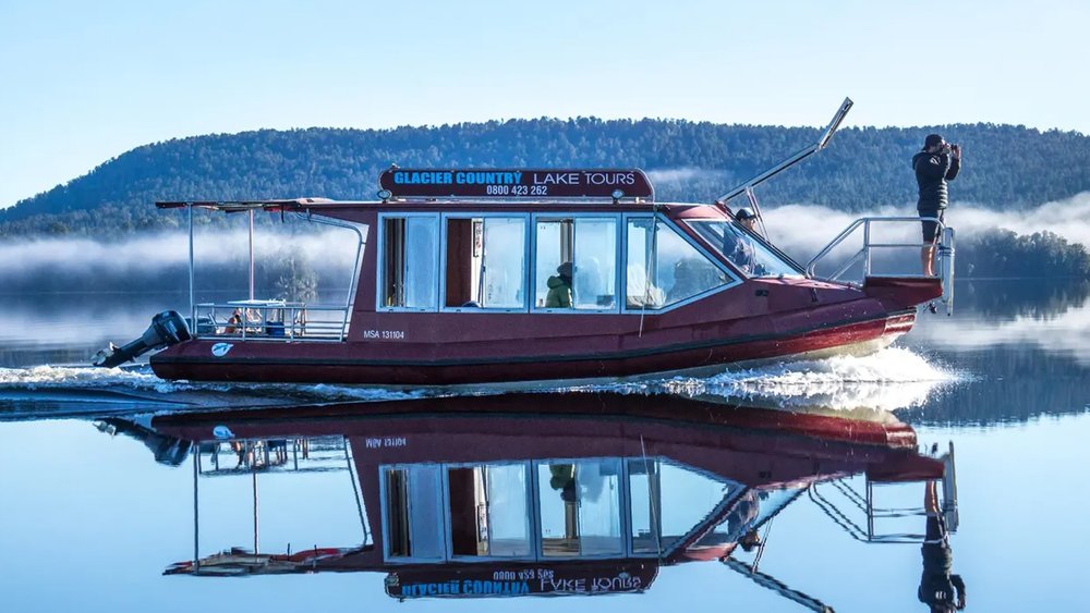 See the snow-covered peaks of the Franz Josef valley reflected on the lake