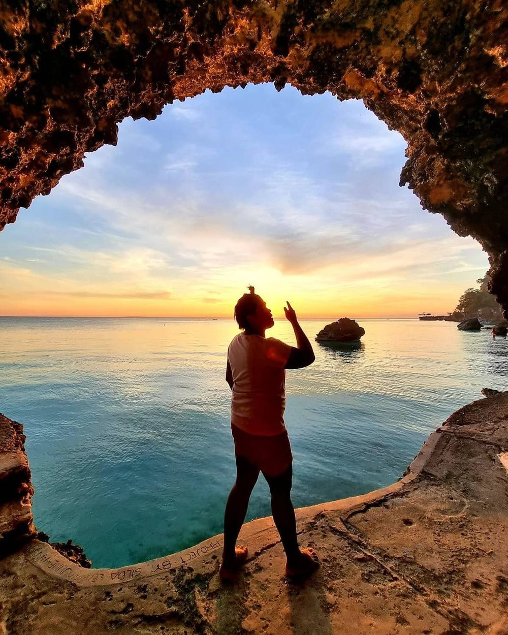 man in cave overlooking sunset in diniwid beach boracay