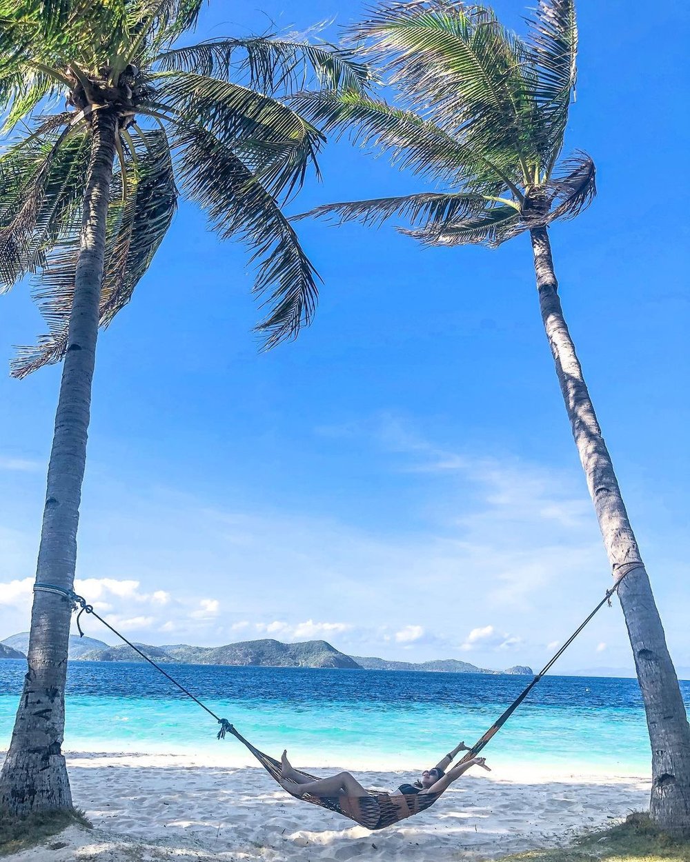 woman resting in hammock between two palm trees