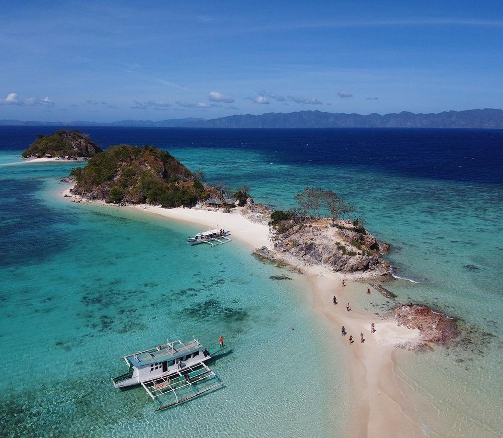 drone shot of long sand bar with rocks and cliffs