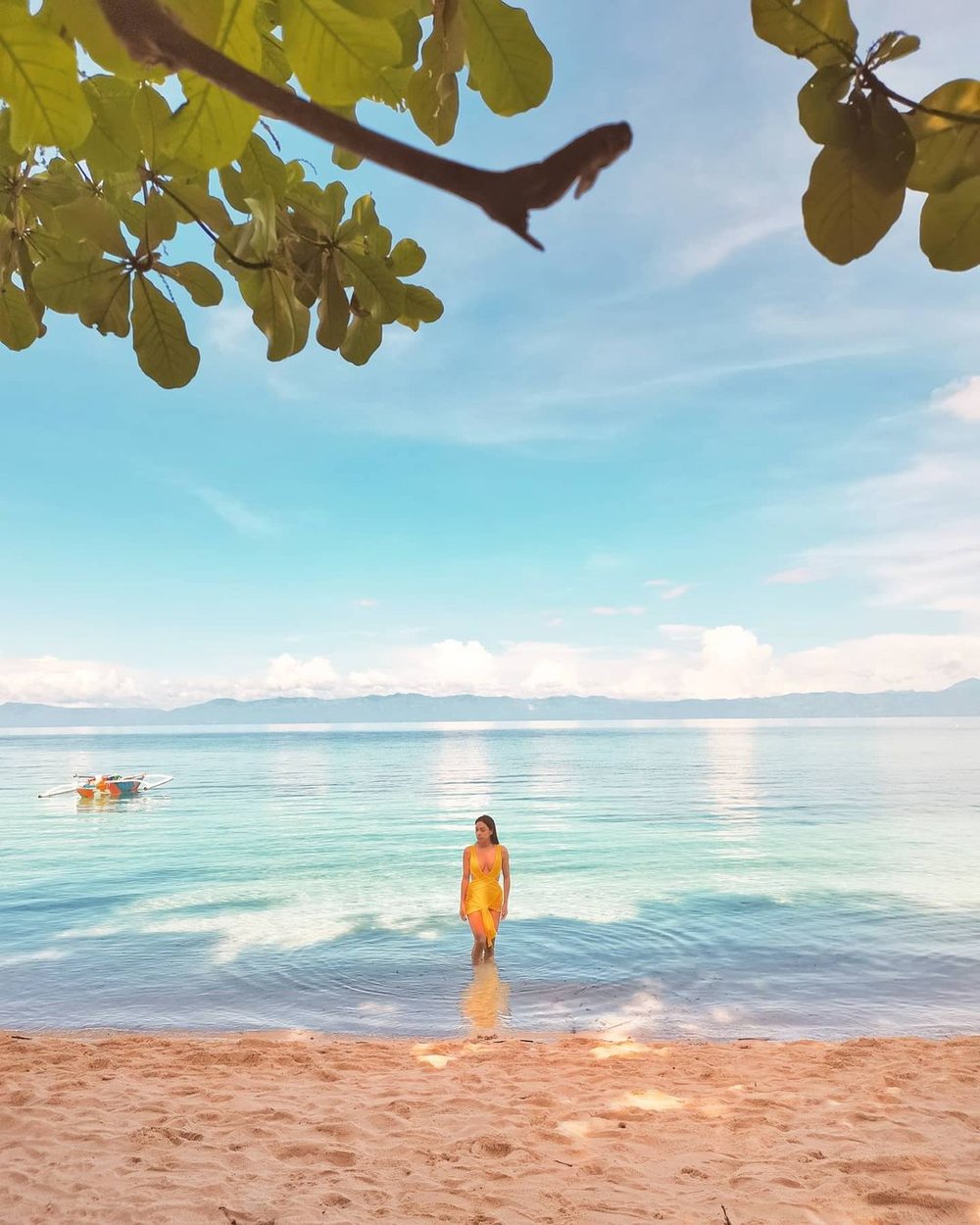woman in yellow standing in shallow waters at the beach