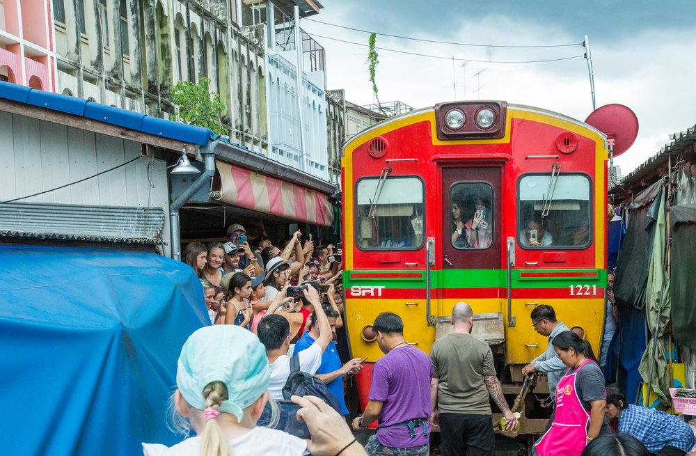 maeklong train chugging along the tracks while vendors wait for it to pass