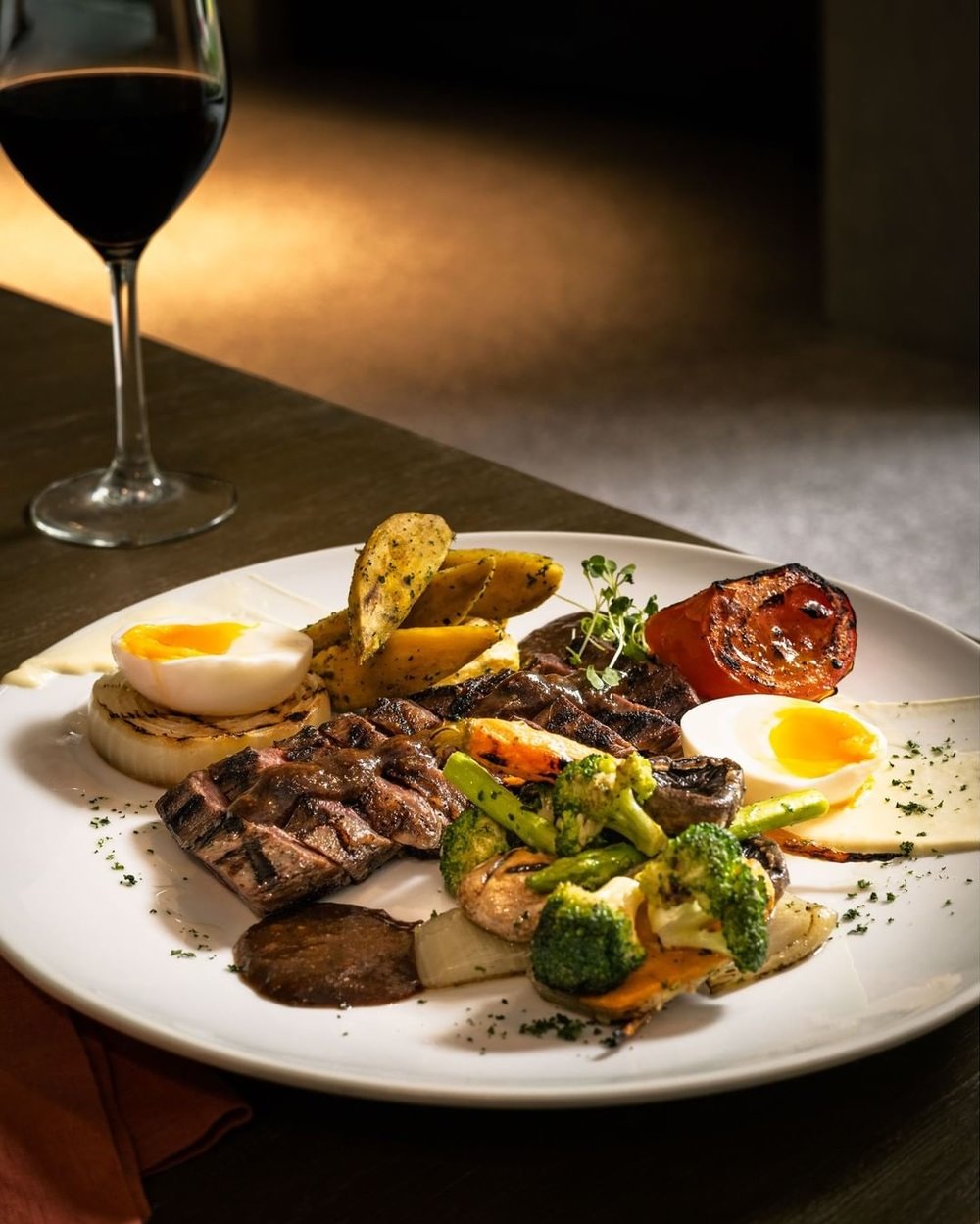 plate of steak, vegetables, and egg next to glass of wine