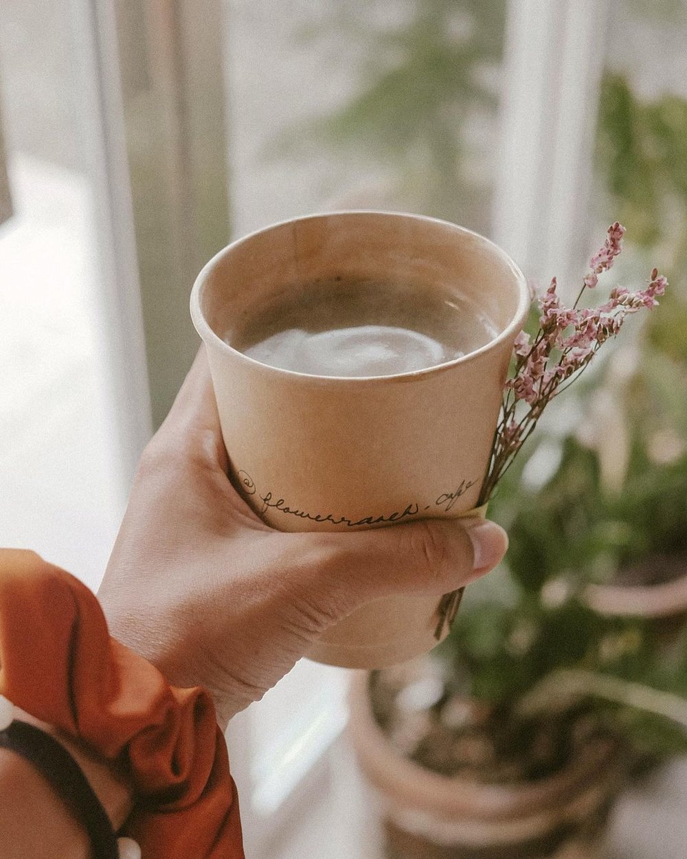 hand holding cup of coffee and dried flower