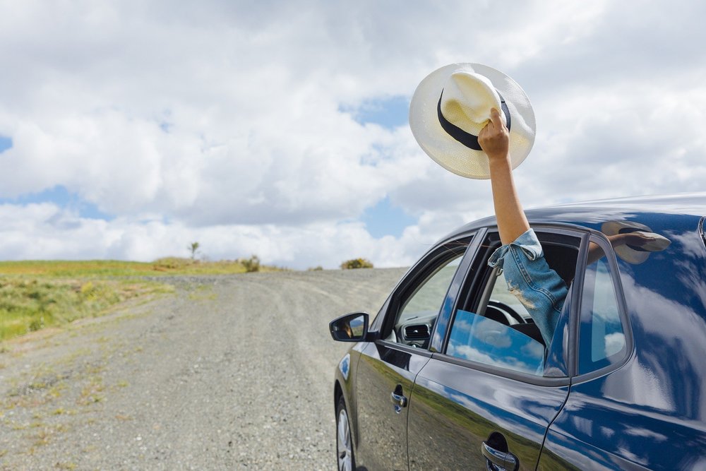 a person inside a car holding a hat outside the backseat side window