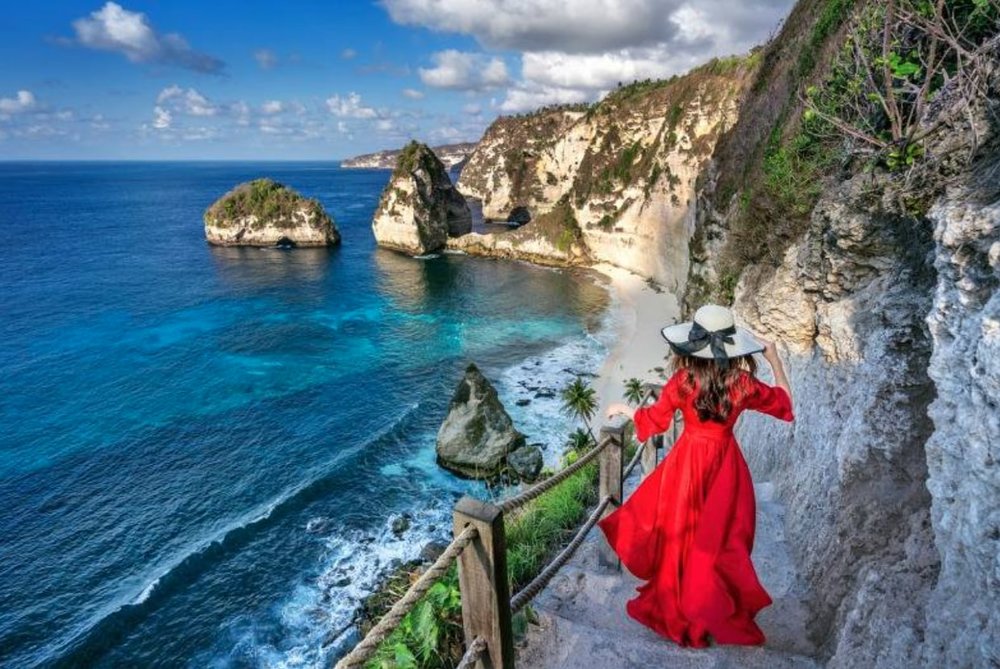 girl in a red dress and white hat climbing down nusa penida