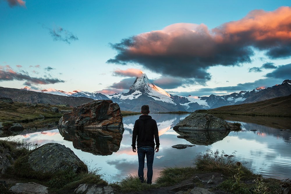a man in a scenic mountain river area in Switzerland looking at a snowy peak from afar