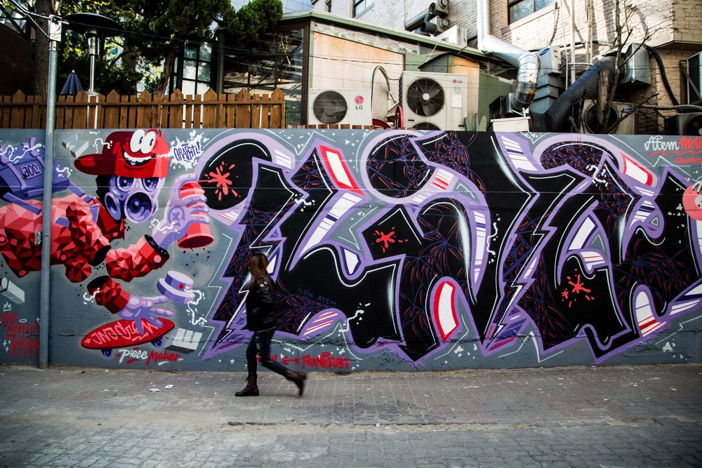 Woman walking beside a vandalized wall in Hongdae