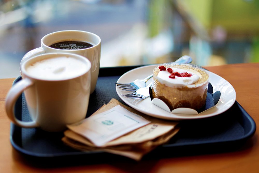 Pastry on a plate beside two cups of coffee