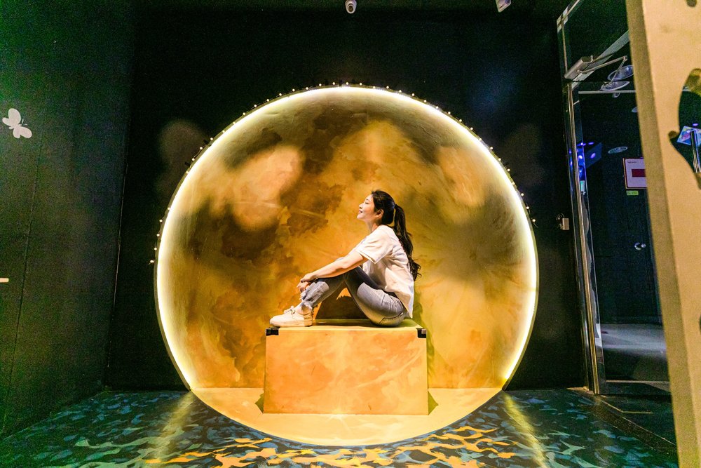 Woman sitting for a photo with one of the pieces inside Alive Museum