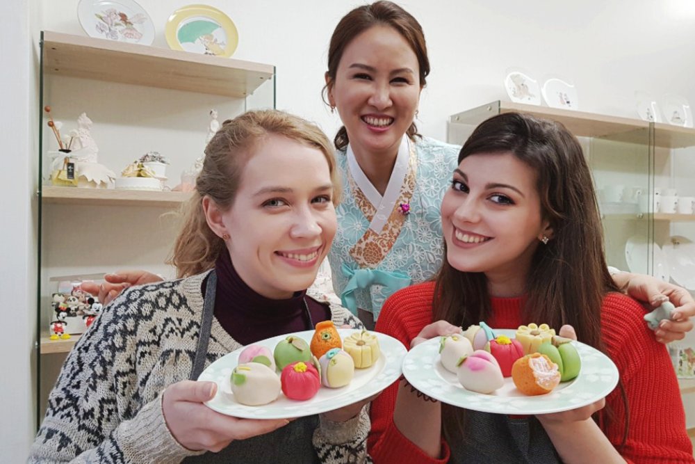 Two girls holding rice cakes and their instructor smiling with them