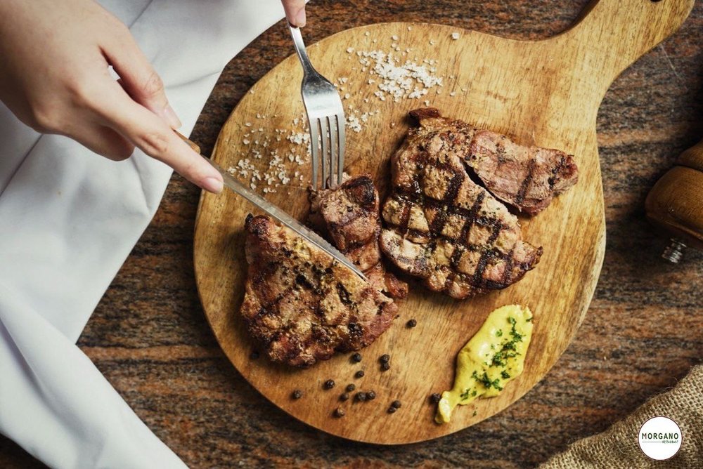 hands cutting steak in a board