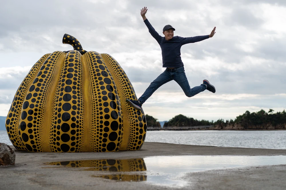 man jumping for joy beside a Yayoi Kusama art installation in Naoshima Island