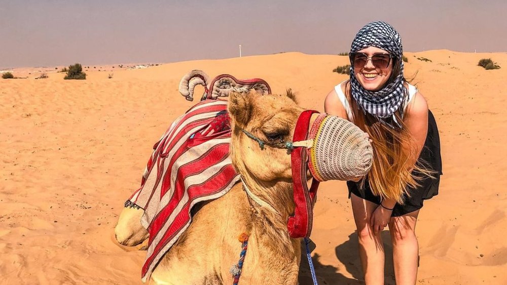 A girl smiling and posing beside a camel