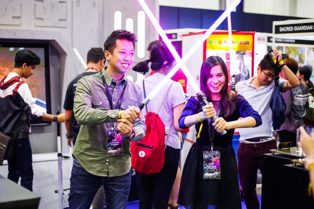 A man and a woman smiling for a photo as they hold their lightsabers