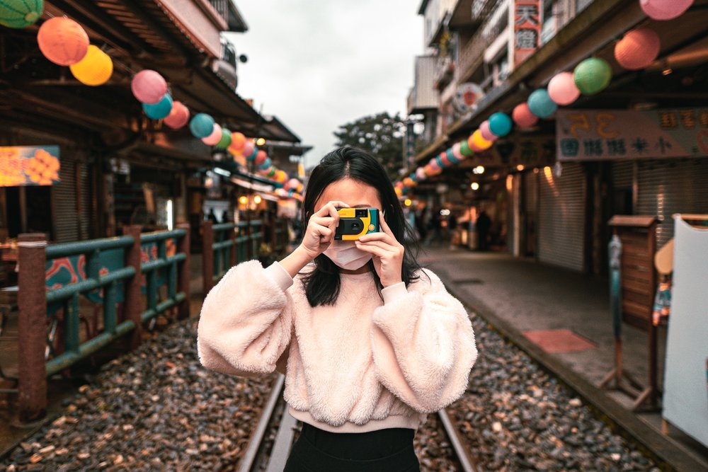 Girl holding a camera while standing on rail tracks