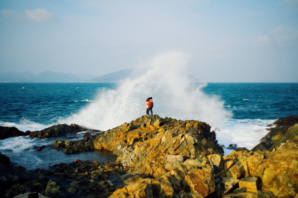 couple watches big wave on rock along cape aguilar