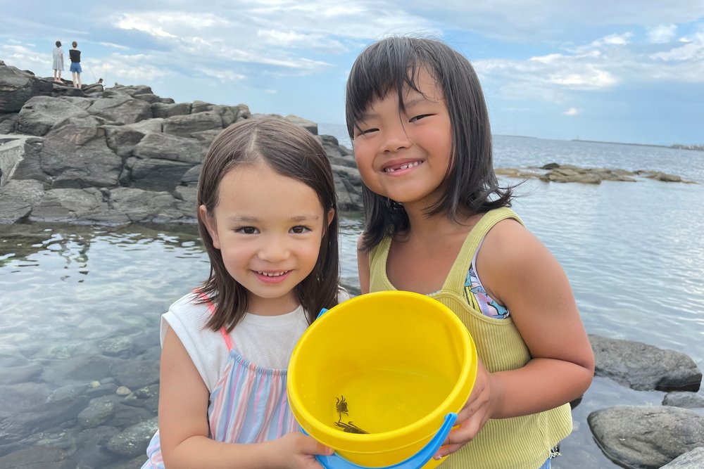 Two girls holding a pail with some small crabs in it