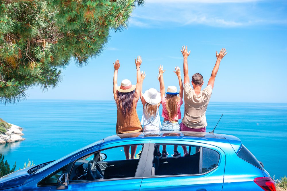 Group of friends sitting on a car with their arms raised
