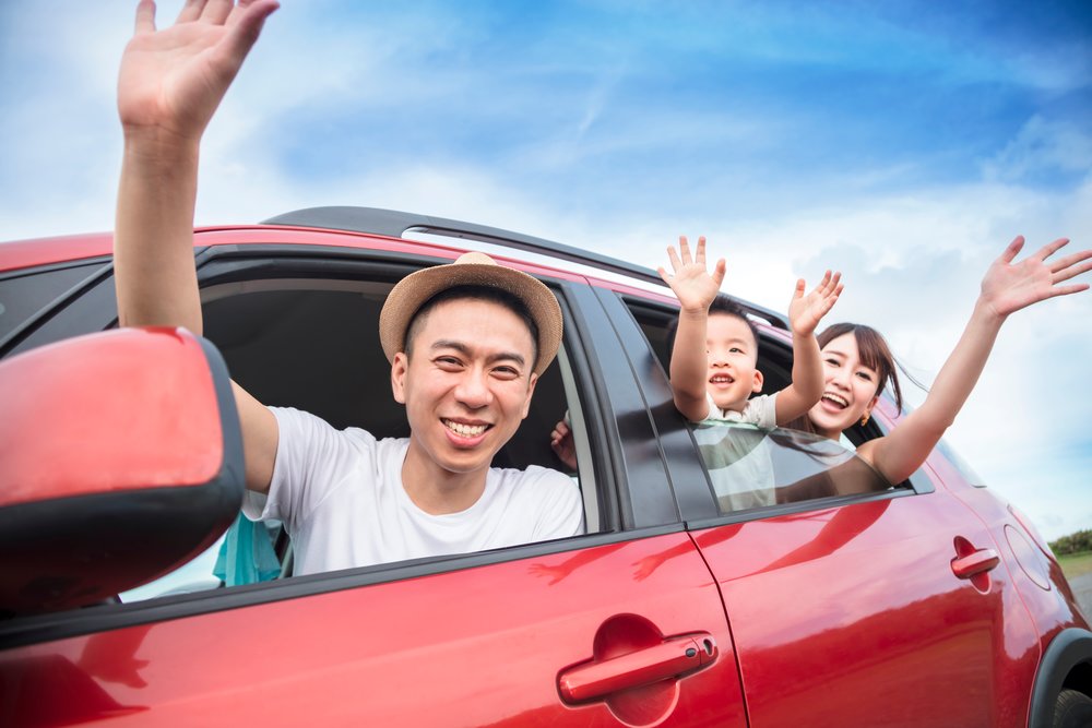 A family happily smiling at the camera while inside a red car