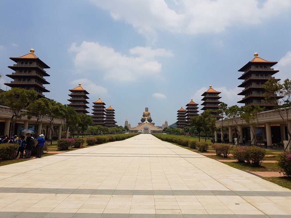 a massive pathway with pagodas on both sides leading up to a large statue of Buddha