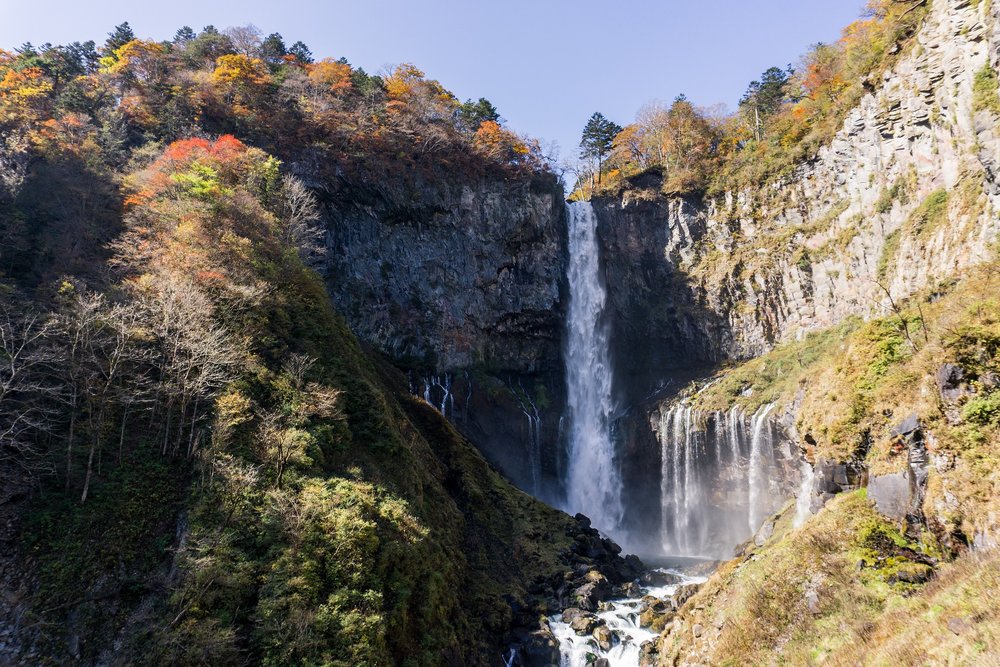 a large waterfall with a cliff and autumn-colored trees