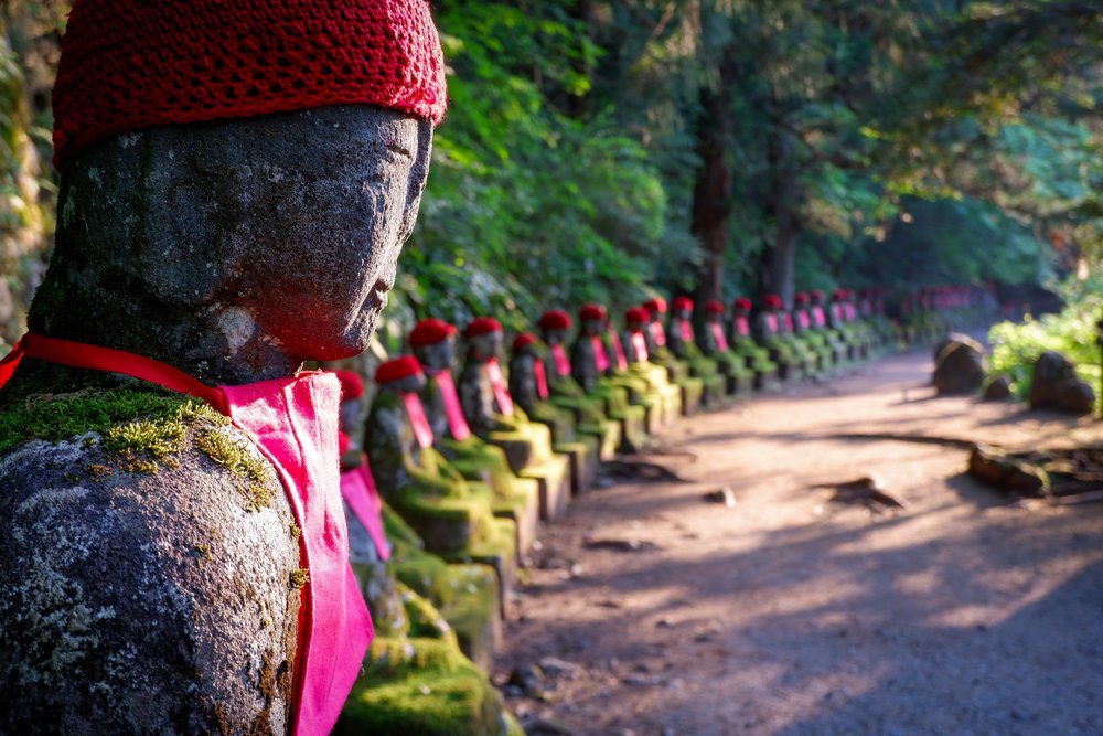 statues lined up in a forest and each wearing red crocheted caps and red bibs