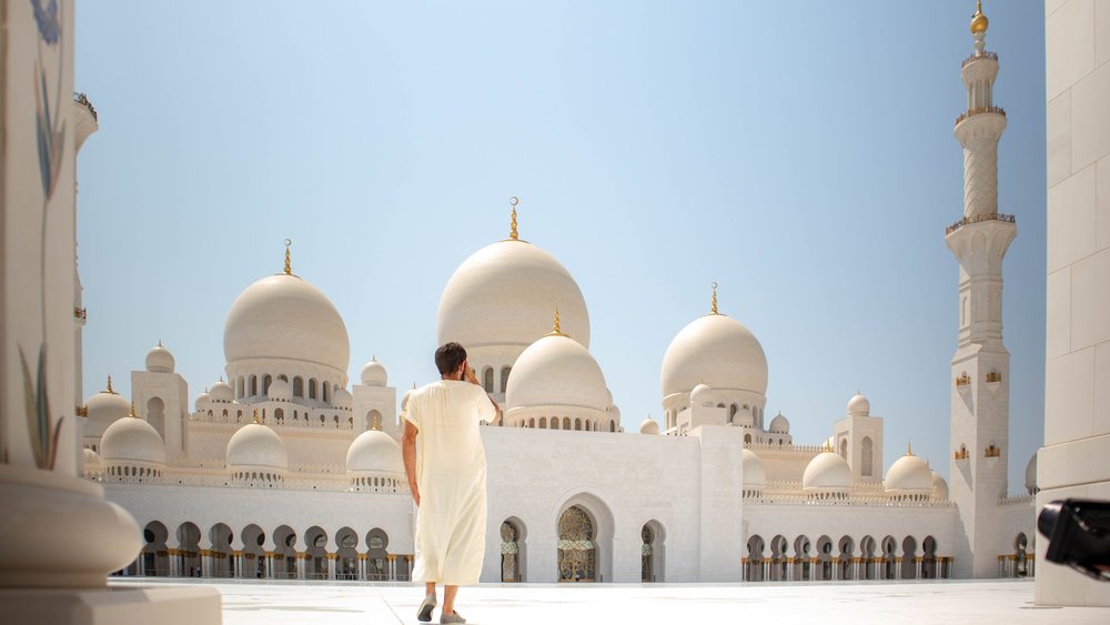 A wide shot of a person wearing white thawb standing at Sheikh Zayed Grand Mosque Center in Abu Dhabi