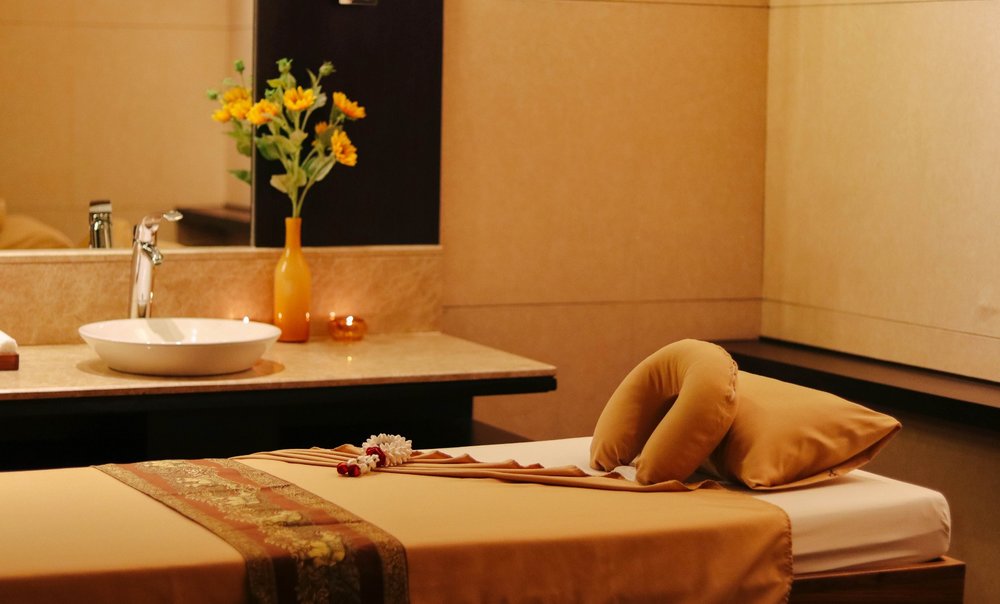 a massage bed with neatly folded sheets and a countertop with a sink, candles, and flowers on the side