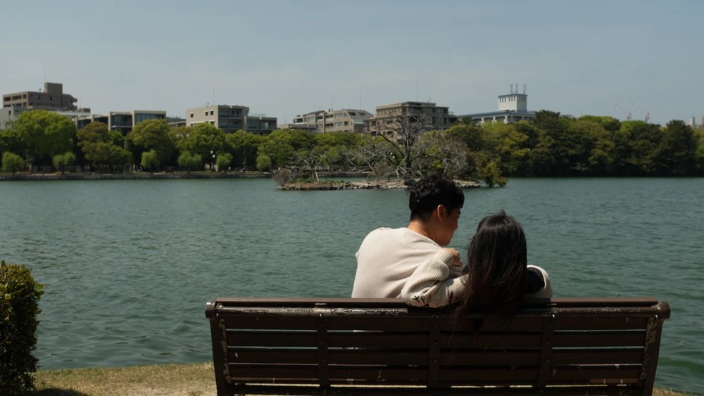 man and woman sitting on bench in front of lake