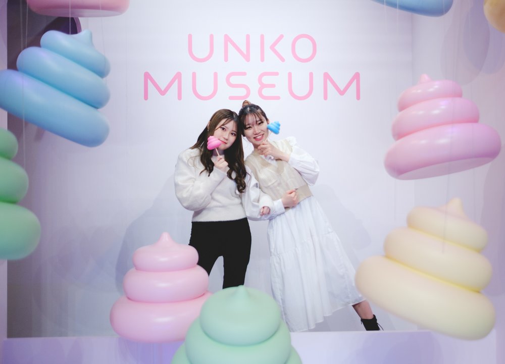 Two girls smiling by Unko Museum sign