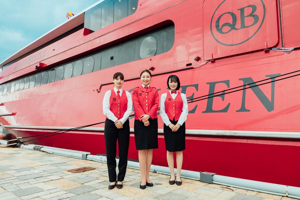 Three girls in crew uniform standing in front of boat