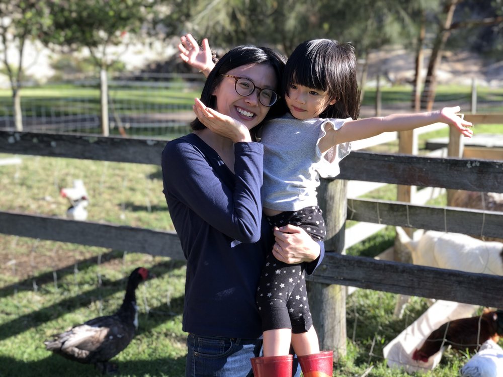mother and daughter pose for a picture with farm animals behind them