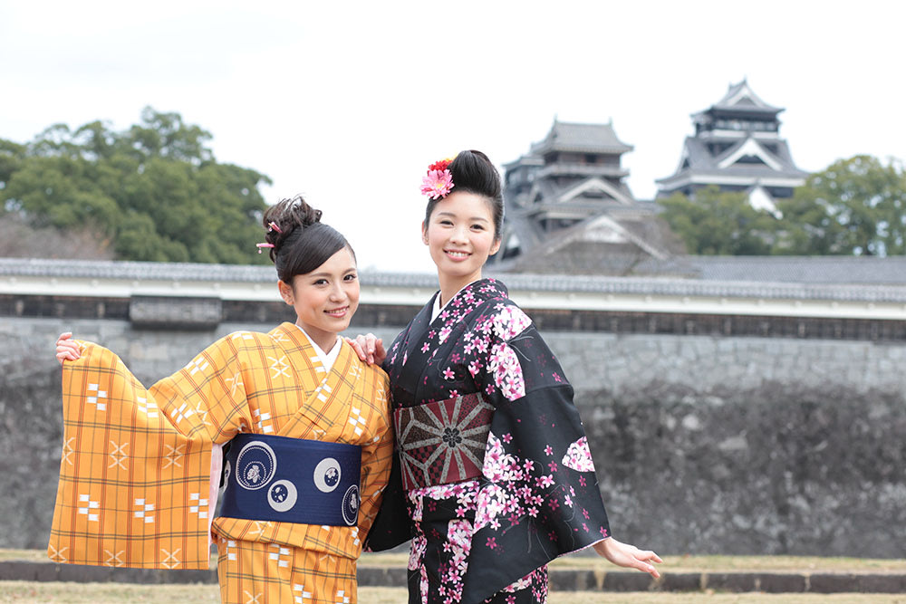 Two young women in kimono posing in front of a Japanese castle