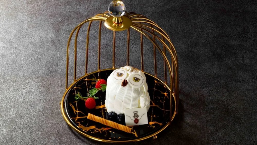An owl-shaped cake decorated with fruits inside a cage