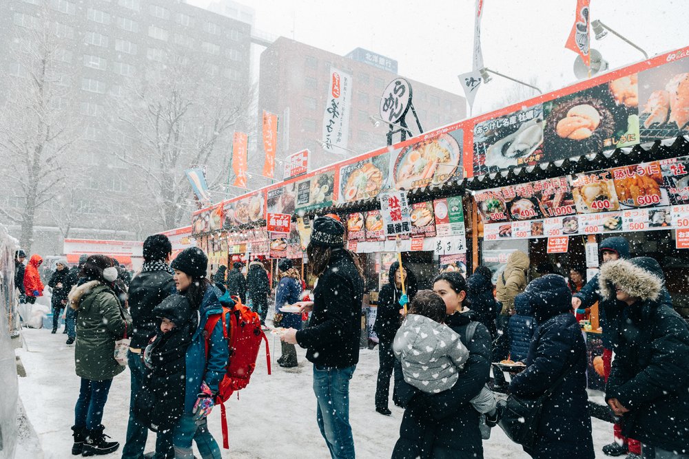 outdoors in Japan with food stalls and people during a snowy day