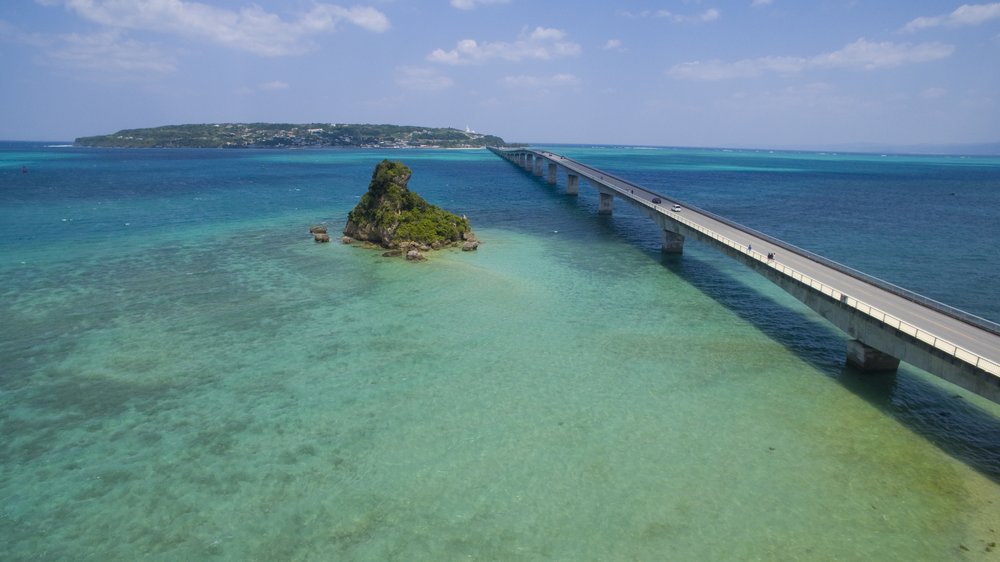 aerial view of a bridge on top of a clear blue body of water in okinawa