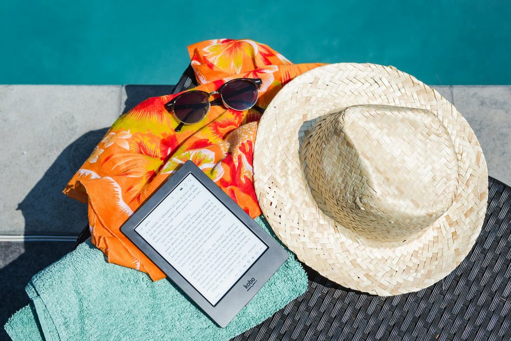 photo of a sun hat, sunglasses, a kindle, and beach towel by the pool