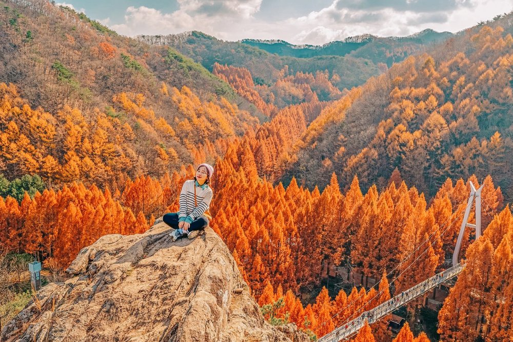 lady sitting on top of a rock with a view of autumn colors in Jangtaesan Recreational Forest
