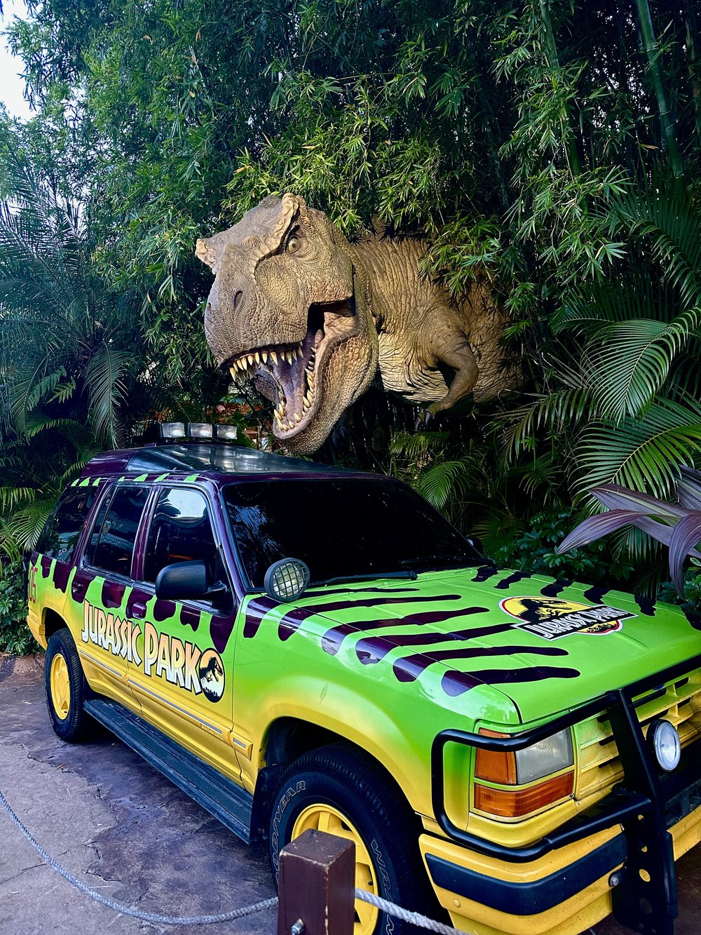 jurassic dinosaur popping out from a bush and on top of a car