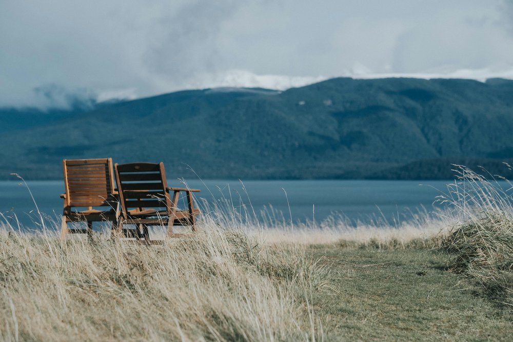 New Zealand South Island Road Trip Itinerary - Two wooden chairs on a grassy field in front of a lake in Te Anau
