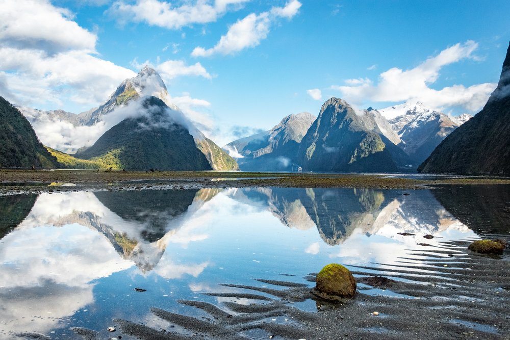 New Zealand South Island Road Trip Itinerary - A reflection of mountains in a body of water at Milford Sound