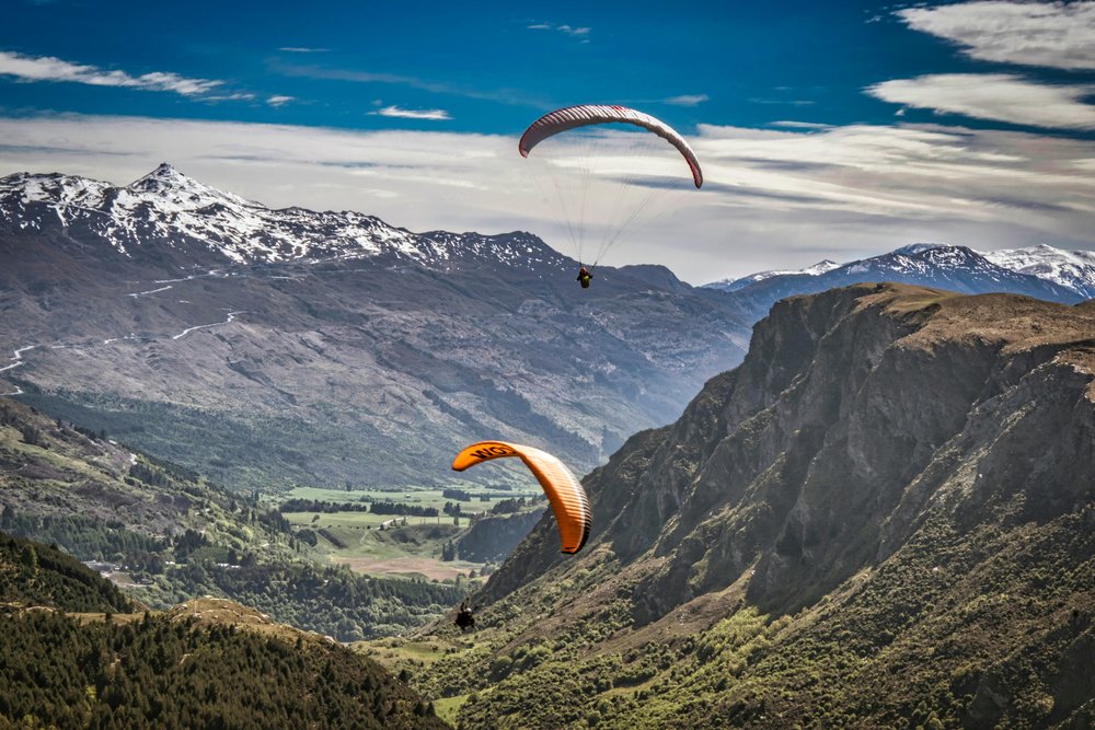New Zealand South Island Road Trip Itinerary - Paragliders soaring above Queenstown with snow-capped mountains in the background