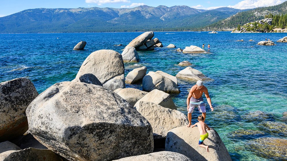 lake tahoe during the day with two people by the lake