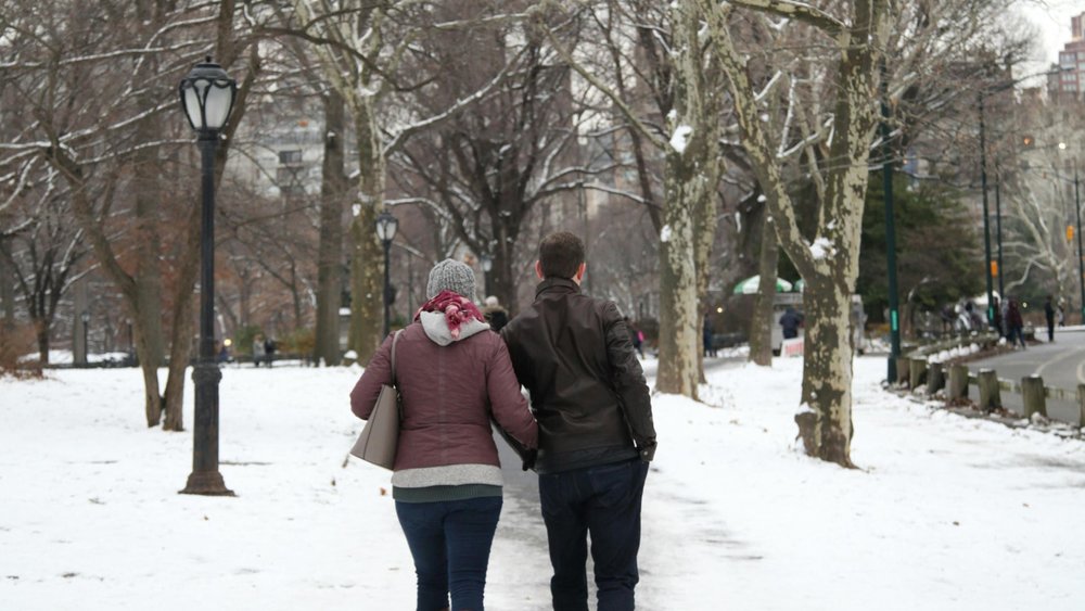 A couple walking down a snowy path in Central Park, New York City during winter.