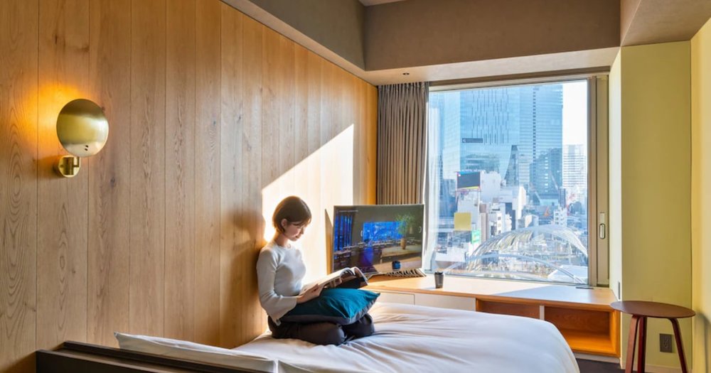 young woman sitting on a bed with a window overlooking the city