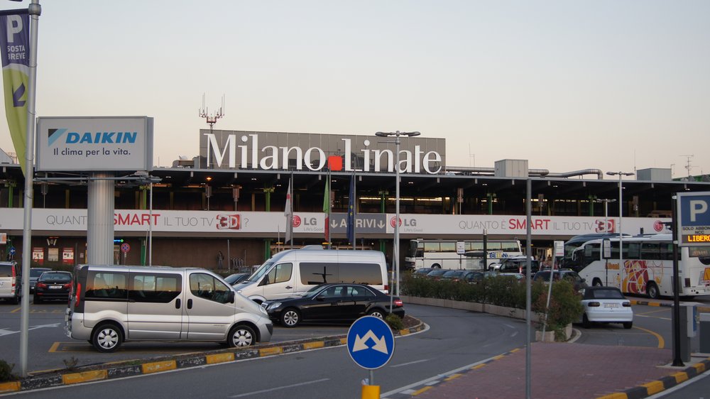 best airport to fly into italy - outdoor shot of airport with cars and vans