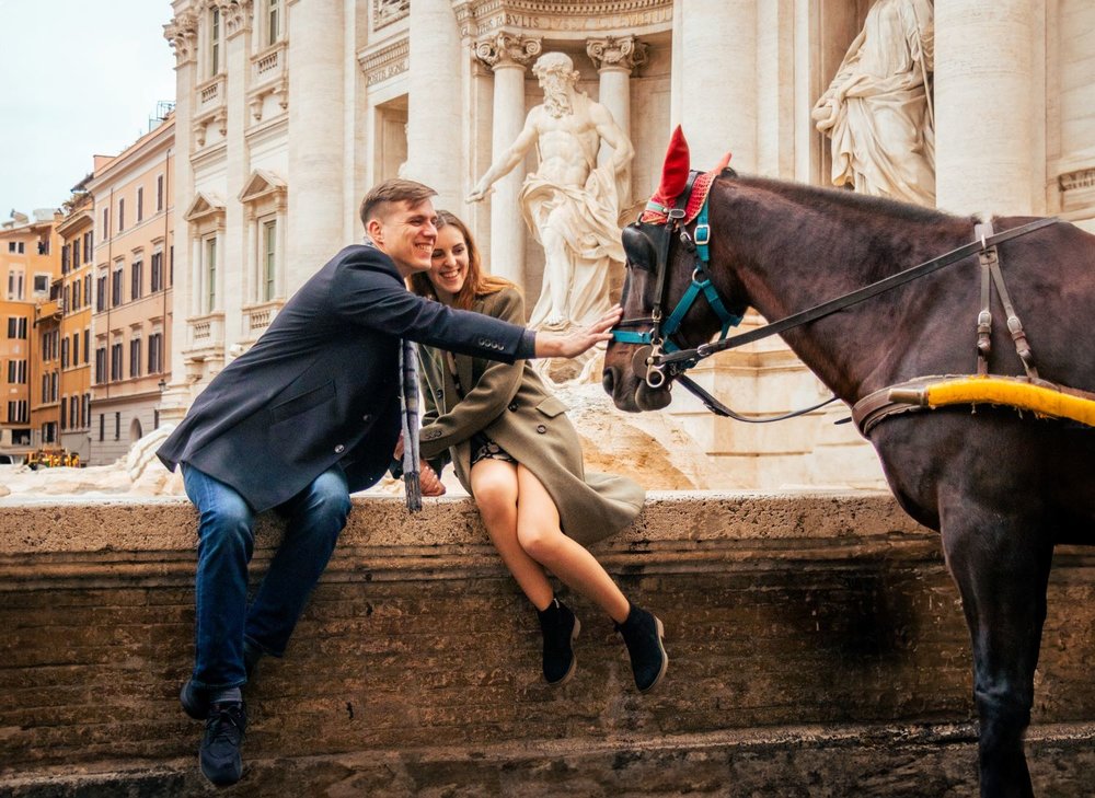 couple posing by the trevi fountain alongside a horse