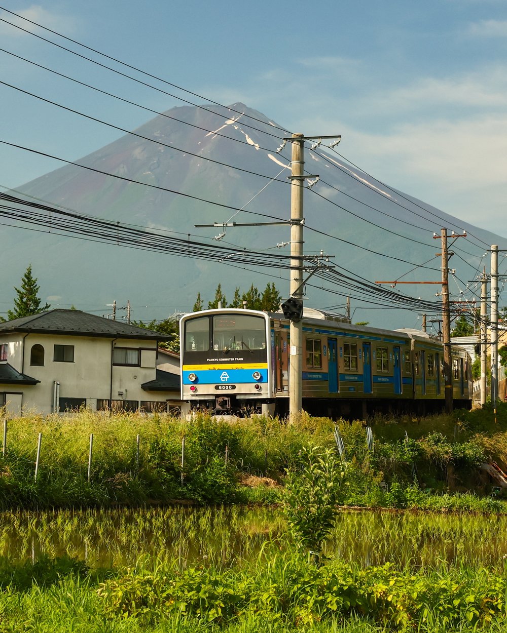 รถไฟ Fujikyu วิ่งผ่านหมู่บ้านชนบท พร้อมฉากหลังเป็นภูเขาไฟฟูจิ