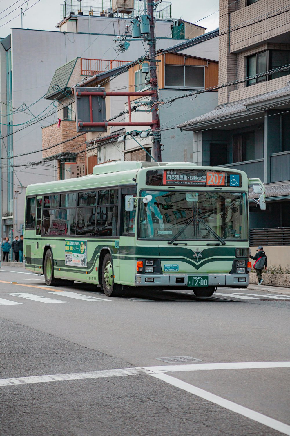 Green Kyoto City Bus driving through a traditional Kyoto neighborhood
